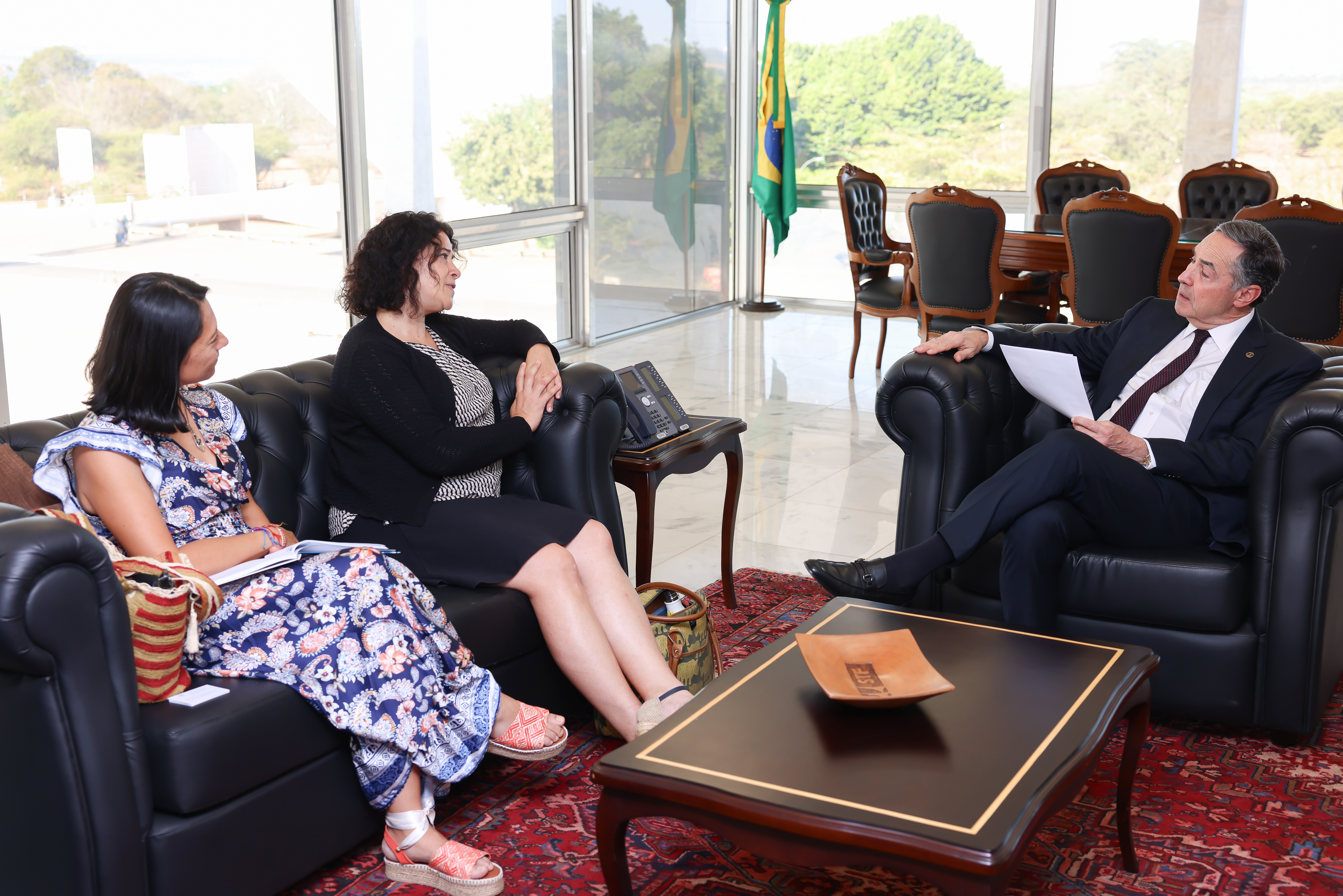 Foto em posição paisagem do ministro Luís Roberto Barroso com as emissárias da ONU em seu gabinete