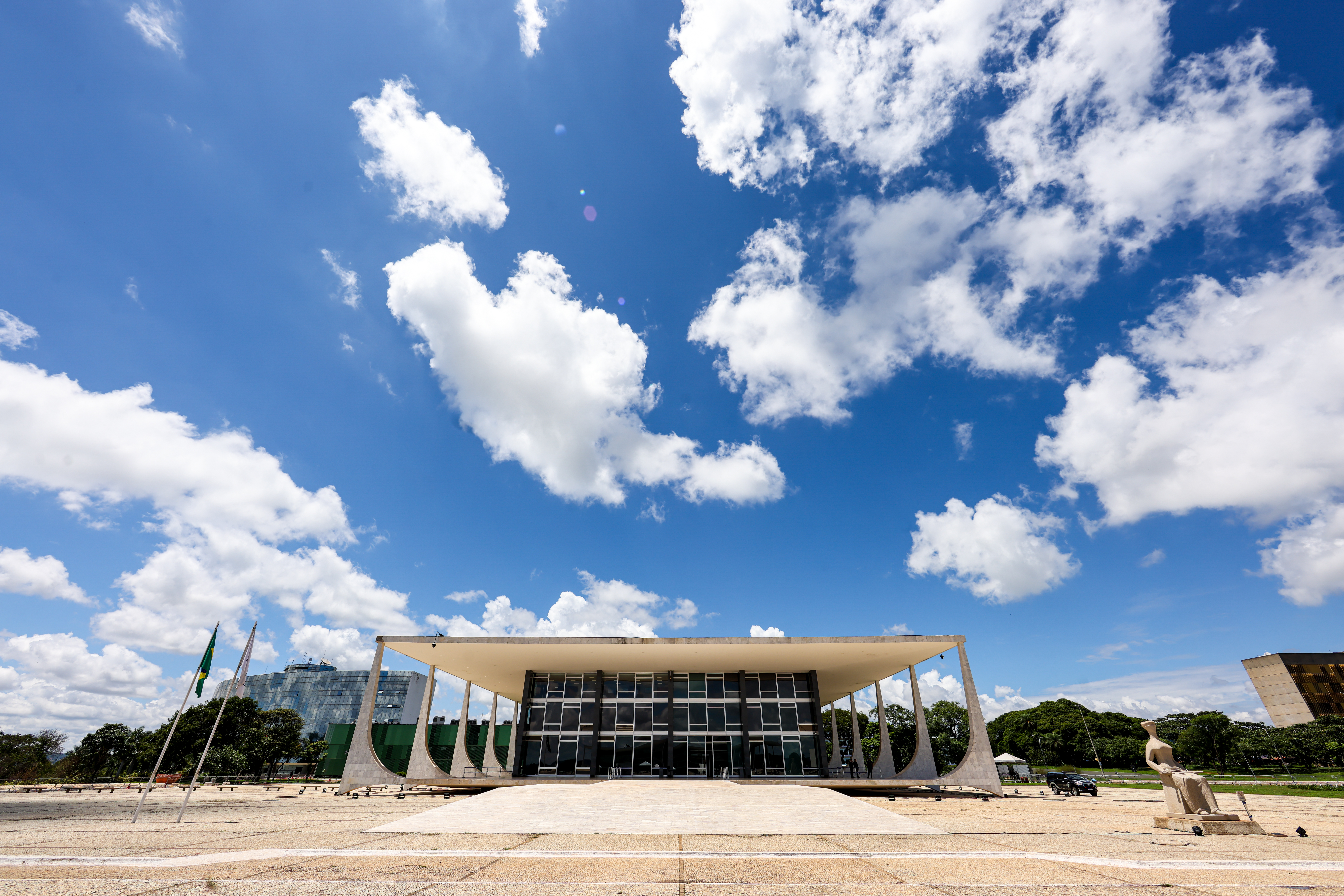 Foto em formato paisagem do prédio do Supremo Tribunal Federal ao centro e ao lado direito a estatua da Justiça e ao fundo o céu azul.