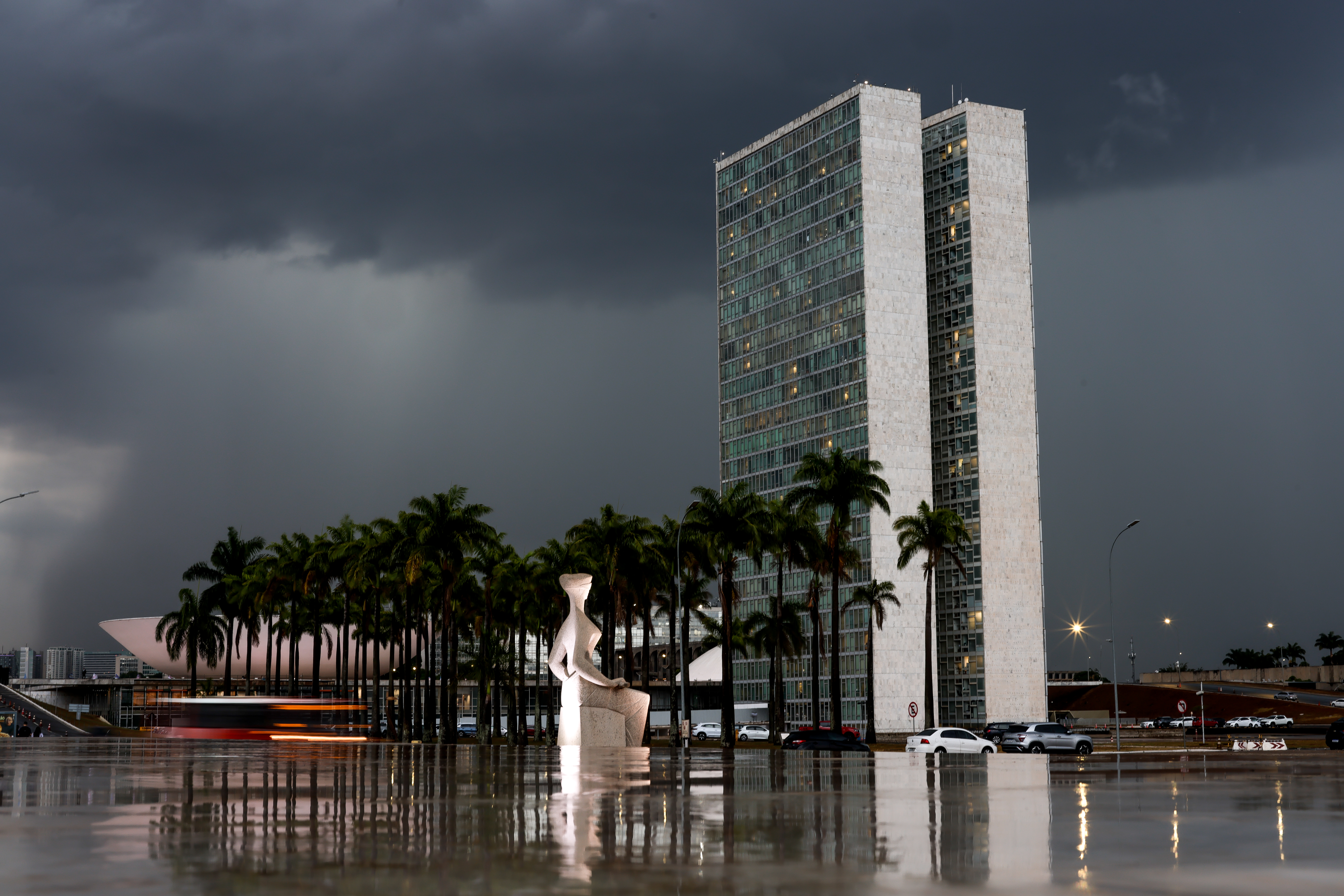 Foto em formato paisagem da estatua da Justiça com o fundo do Congresso Nacional e ao fundo o céu nublado de chuva.